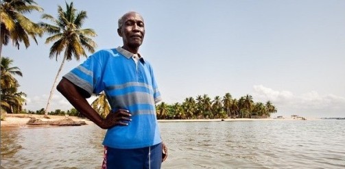 Man at Azizakpe, Ada, Ghana, standing in flood water where his home used to be. Image credit: Nyani Quarmyne